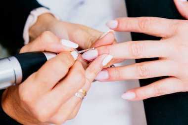 Güzellik uzmanının kadın bir müşterinin tırnak etlerini güzellik merkezinde özel bir aletle düzeltirken çekilmiş bir fotoğrafı. Beyaz tırnaklar, hindistan cevizi rengi. Kavram: iyi olmak