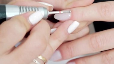 4K Güzellik Uzmanı 'nın bir kadın müşterinin tırnak etlerini güzellik merkezinde özel bir aletle düzelttiği videoyu kapat. Beyaz tırnaklar, hindistan cevizi rengi. Kavram: iyi olmak