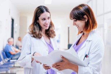 Two young happy female doctors stand in a hospital corridor. Women empowerment. Medical records checking. Positive atmosphere in workplace. White background for copy space clipart