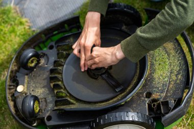 Lindesnes, Norveç - 09 Ağustos 2022: Yeşil kazaklı bir kişi bir robot çim biçme makinesinin bıçağını değiştiriyor.