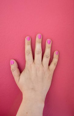 Pembe bir duvarda pembe ojeli sağ el..