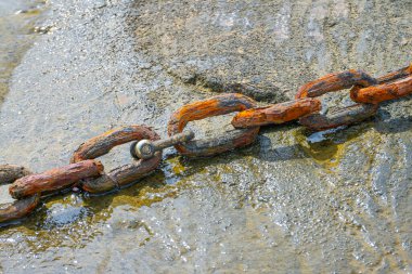 Old rusty metal chain on wet ground.