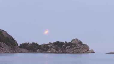 Kanlı ay denizin ve kayalıkların üzerinde yükseliyor.