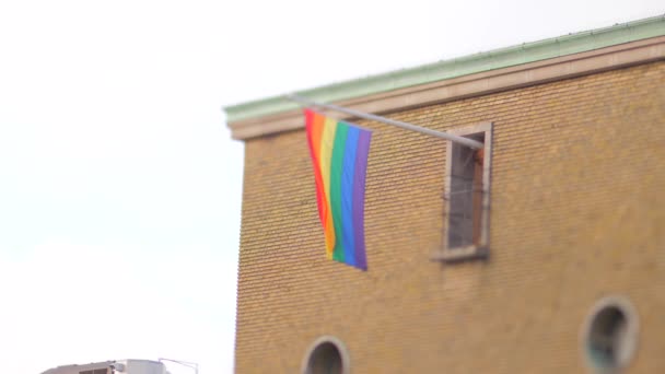 レインボーフラッグがレンガ造りの建物の旗竿に垂直にかかっています — ストック動画