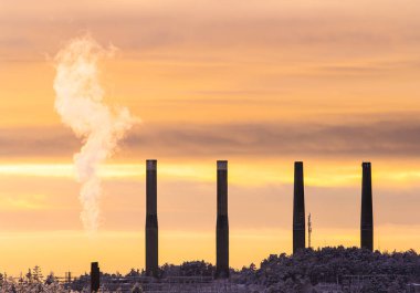 Uzaktaki dört bacayla birlikte bir bacadan buhar yükseliyor..