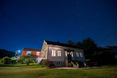 Lindesnes, Norveç - 05 Ağustos 2022: Yukarısında görünür yıldızlar bulunan geleneksel bir Norveç ahşap evinin gece fotoğrafı.