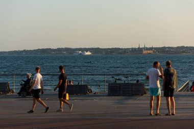 Helsingborg, İsveç - 17 Temmuz 2021: İnsanlar sahilde yürüyüş yapıyor. Arka planda feribot ve Helsingor.