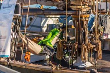 Oslo, Norveç - 20 Temmuz 2014: Peraon eski ahşap bir yelkenli gemide modern yeşil bir uyku tulumunda uyuyor..