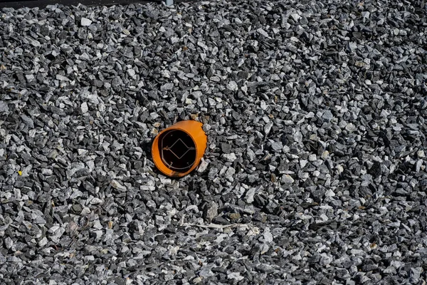 Orange drain pipe sticking out of a stone pile by a ditch.