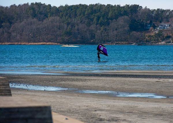 stock image Gothenburg, Sweden - March 13 2022: Person in the water by a beach getting ready to wing foil.