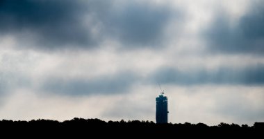 Silhouette of tall skyscraper under construction behind a forest.