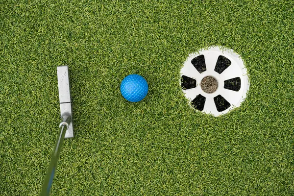 Miniature golf putter by blue ball and hole.