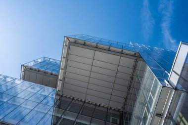 Çatı çıkıntısı ve mavi gökyüzü modern bir binanın cam cephesine yansıyor..