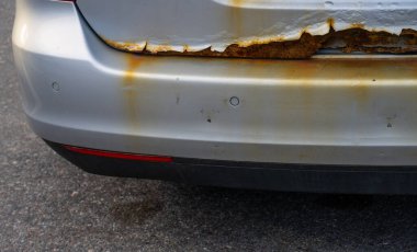 Gri bir arabanın paslı arka kapağı.