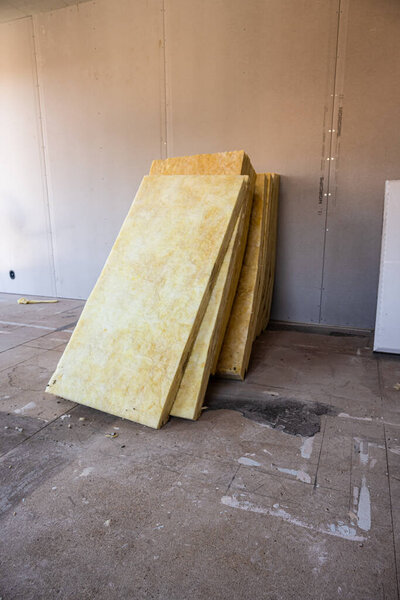 Glass wool insulation stacked by a wall.