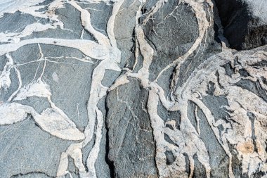 Koyu ve açık gri migmatik kayalar deniz tarafından kumla kaplanmış..