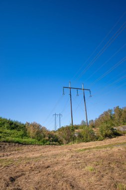 Kuru bir çim tarlasının üzerinde iki büyük elektrik voltajı direği..
