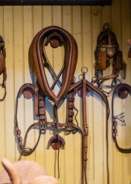 Duvarda asılı duran eski at koşumları.