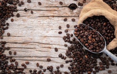 Background of dark roasted coffee beans with scoops setup on wooden background with copy space.