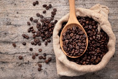 Background of dark roasted coffee beans with scoops setup on wooden background with copy space.