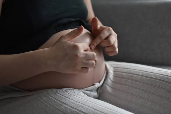 pregnant woman touching belly button on belly