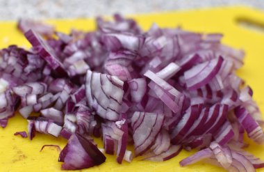 Sarı kesme tahtasına kırmızı soğan dilimlenmiş.