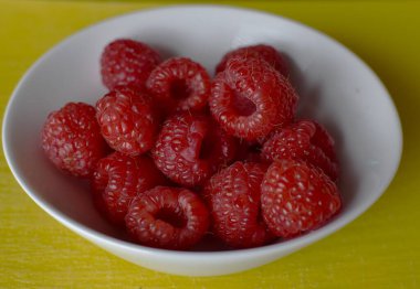 Küçük beyaz bir fincanda olgun ahududular.