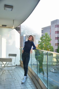 Siyah elbiseli genç kadın balkonda duruyor.