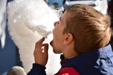 Çocuk dışarıda pamuk helva yiyor.