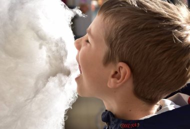 Çocuk dışarıda pamuk helva yiyor.