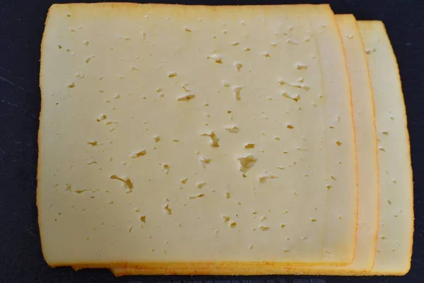 スライスしたチーズは黒い板の上にあり — ストック写真