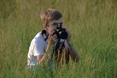 Çocuk çimenlerde refleks kamerasıyla oturuyor.