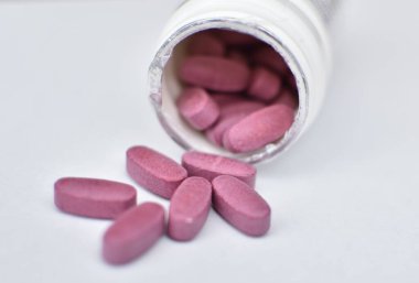 Vitamin hapları beyaz bir arka planda poastik bir şişeye saçılmış.