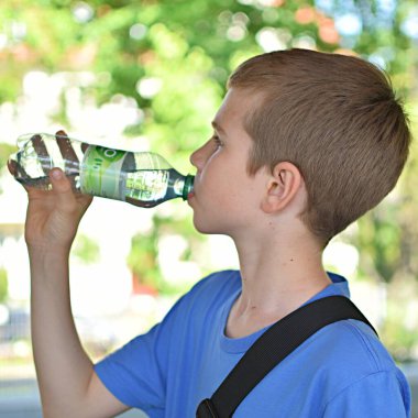 Çocuk açık havada plastik bir şişeden su içiyor.