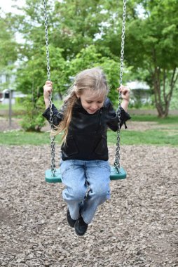 Siyah ceketli sarışın kız salıncakta sallanıyor.