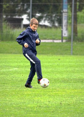 Futbol sahasında futbol topunun peşinden koşan bir çocuk.