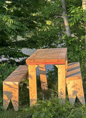 Ev yapımı masa ve yeşil ağaçların altında çimlerde iki bank.