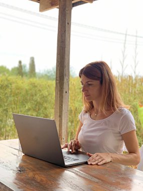 Genç bir kadın dışarıda masada oturuyor ve dizüstü bilgisayarına bakıyor.