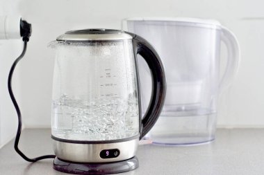 Su bir çaydanlıkta kaynıyor ve yakınlarda bir su filtresi var.