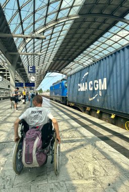 Berlin, Almanya, 06.18.2025Man platformda tekerlekli sandalyede bir yük treni geçerken