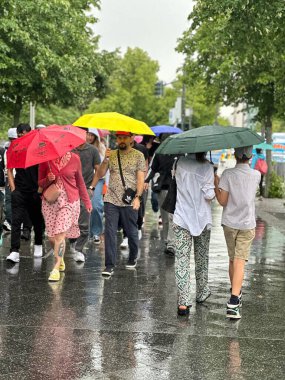 Berlin, Almanya, 6 Temmuz 2025 Yağmurlu bir günde renkli şemsiyeler altında yürüyen insanlar.
