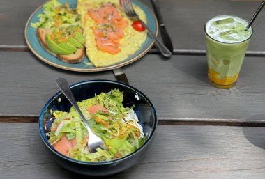İki tabak avokado ve kırmızı balık tabağı bir bardak kibrit mangoyla servis edilen ahşap bir masada metal pipetle servis edilir. Doğal ışık altında sağlıklı bir kahvaltı..