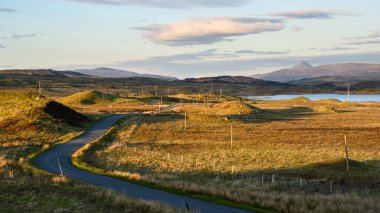 Empty road to Rannoch Moor train station in Scotland during sunset with lake and mountains in the background
