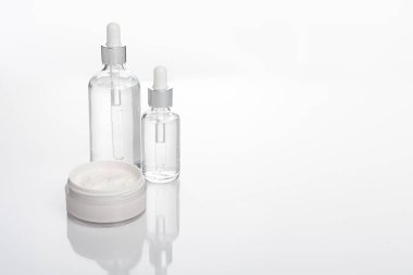 Beyaz tabanı ve beyaz krema şişesi olan şeffaf damla şişesi.