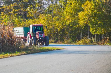 Yolda karavanı olan kırmızı traktör. Sonbaharın başı.