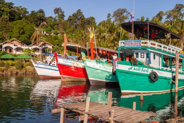 Bereketli tropikal ormanın yanındaki ahşap iskeleye yanaşan renkli balıkçı tekneleri, Koh Chang, Tayland