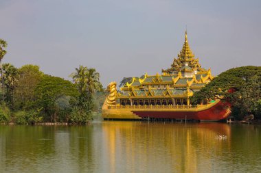 Altın Karaweik Sarayı manzarası, Yangon 'daki Kandawgyi Gölü' nde yüzen bir mavna, yemyeşil ağaçlar ve huzurlu bir yansıma..