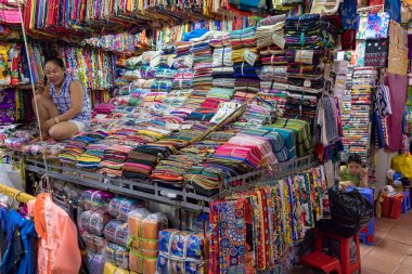 Markette renkli kumaş yığınlarının arasında oturan kadın.