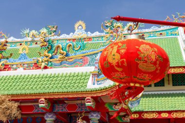 Canlı kırmızı bir Çin feneri yeşil çatılı geleneksel bir tapınağın önünde asılı duruyor..