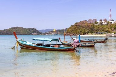 Geleneksel Tayland uzun kuyruklu tekneleri yeşil bir adanın kıyısındaki sığ bir tropikal körfeze demirlediler.
